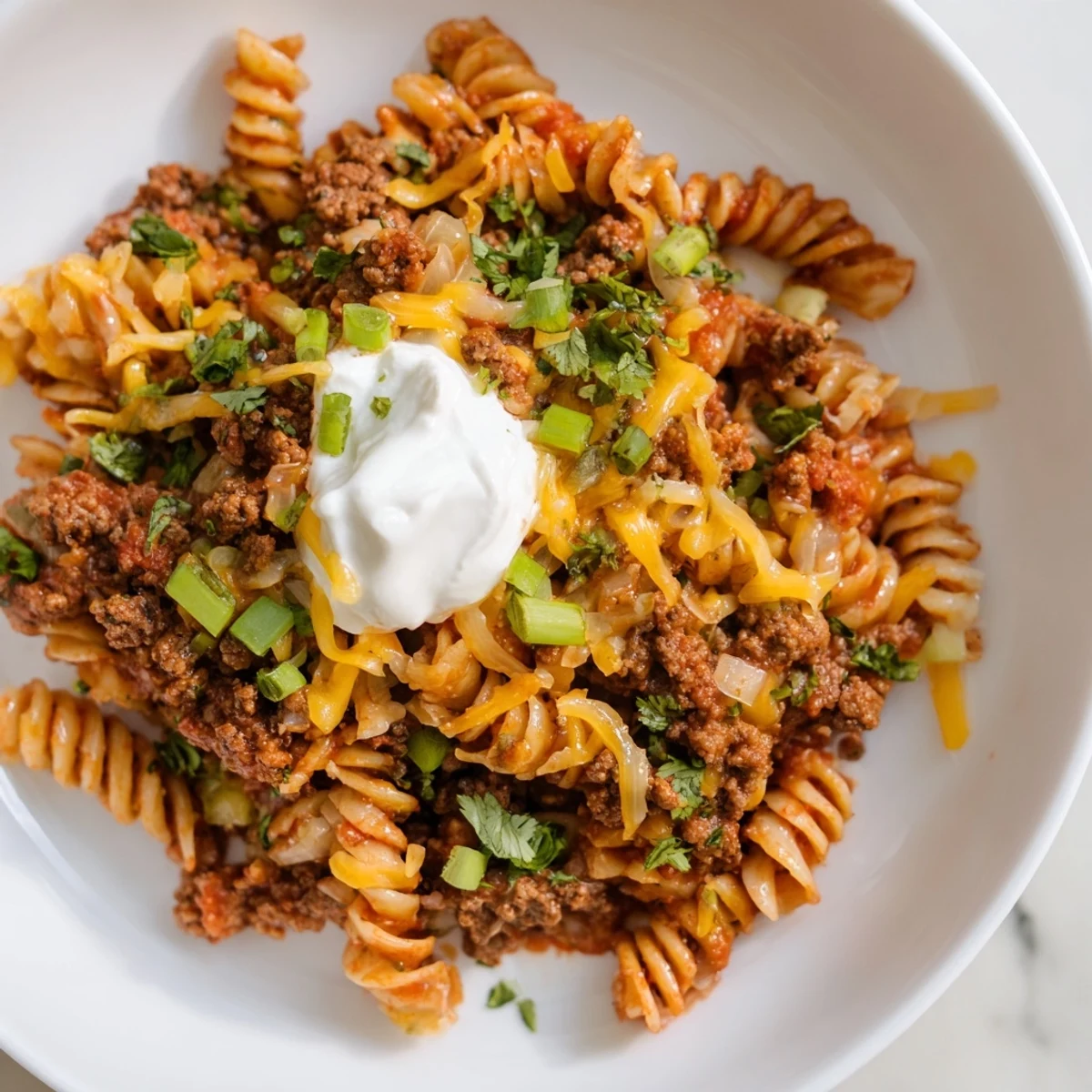Imagine the cheesy goodness of this Easy Beef Enchilada Pasta, garnished with cilantro and sour cream.