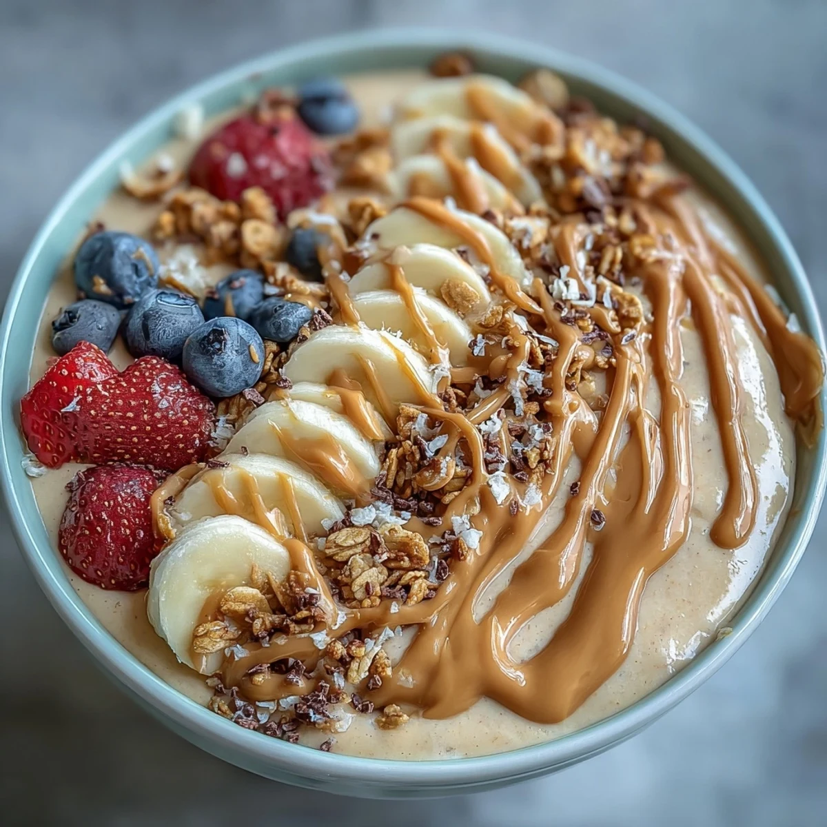 Creamy vegan smoothie bowl with peanut butter, banana, and protein, topped with fresh berries and crunchy granola for a healthy breakfast.