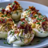 Savory deviled eggs with bacon bits and ranch dressing, served chilled on a white platter with fresh herbs.