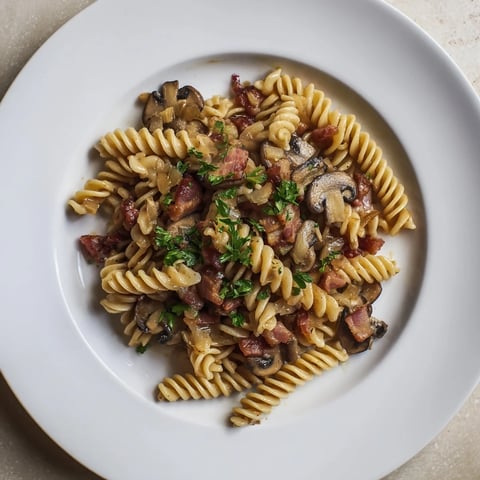 Steaming bowl of fusilli with bacon, onions, and mushrooms, a comforting Italian-inspired dinner.