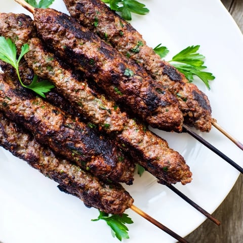 Smoky, char-grilled Iraqi Kebab Tikka skewers, served on flatbread with fresh herbs and lemon.