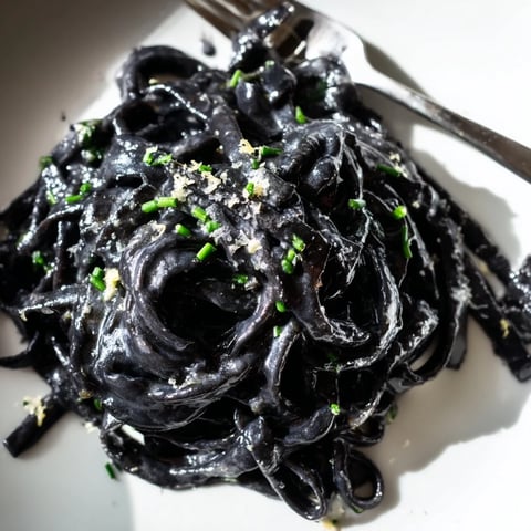 Glossy black squid ink pasta coated in silky cream sauce, garnished with fresh chives and lemon zest.