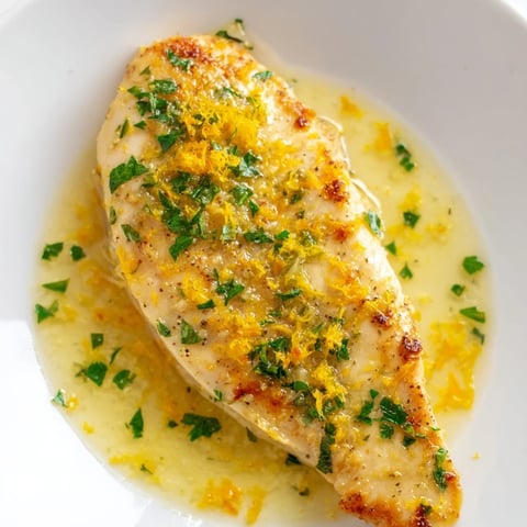 Golden-brown Lemon Pepper Chicken breasts glistening with a vibrant butter sauce, garnished with fresh parsley and lemon zest, ready to serve over rice.  
