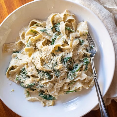 Steaming creamy spinach garlic noodles twirl on a fork, with wilted greens and melted Parmesan.  