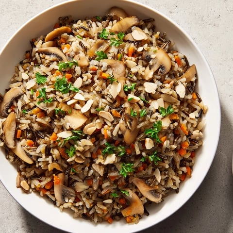 Wild rice and mushroom pilaf steaming in a white bowl, garnished with fresh parsley and toasted almonds.