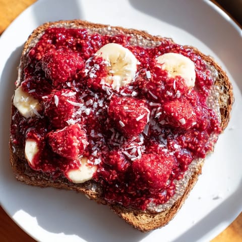 Fresh raspberries and sliced bananas adorn the beautiful raspberry chia jam toast, ready to enjoy.