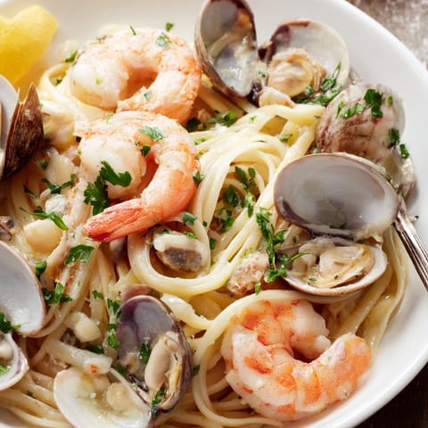 Fresh linguine strands are tossed with tender clams and a sprinkle of parsley, highlighting the vibrant seafood in a golden, aromatic broth.