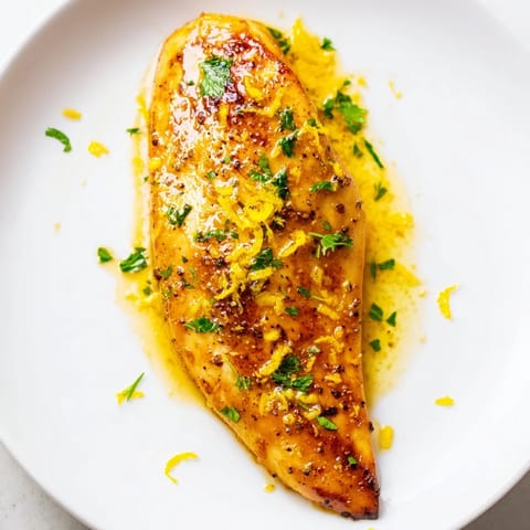Juicy Lemon Pepper Chicken breasts sizzling in a skillet with melted butter, garlic, and lemon juice, creating a golden pan sauce.  