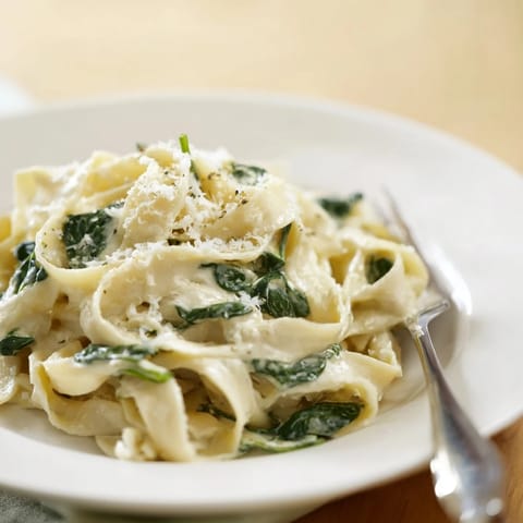 A skillet of creamy spinach garlic noodles, sautéed garlic and onions simmering in rich cream.  