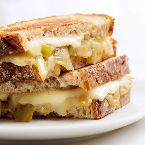 A close-up of the Havarti & Caramelized Leek Grilled Cheese shows gooey cheese and tender leeks between crisped, golden-brown bread.  