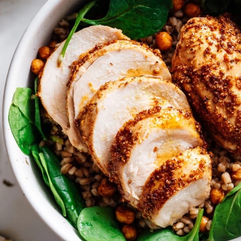 Overhead view of a nutritious Lemon Tahini Chicken Power Bowl with chickpeas, diced cucumber, and fluffy farro topped with a rich tahini drizzle.