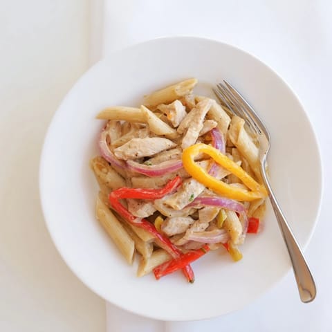 Creamy Cajun Chicken Pasta Lite served in a white bowl, garnished with fresh parsley and red bell pepper slices for a colorful main dish.