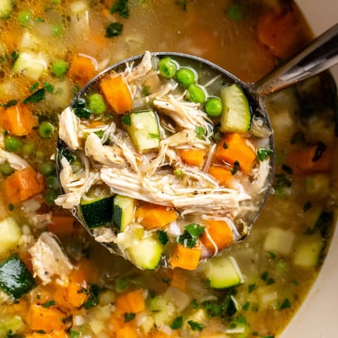 A comforting bowl of Spring Garden Chicken Soup, loaded with carrots, zucchini, and herbs.