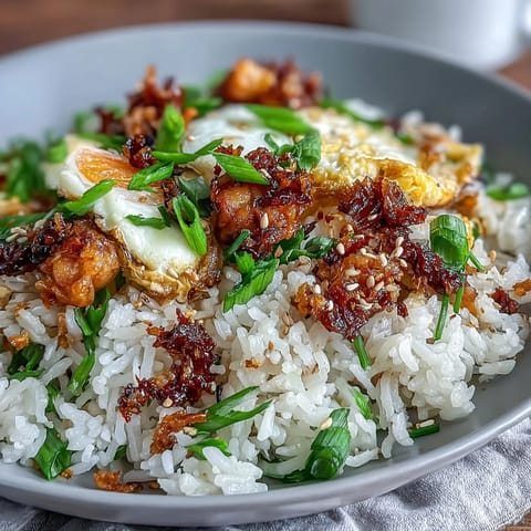 A sizzling skillet of chili crisp egg fried rice with golden scrambled eggs, vibrant green scallions, and a spicy chili oil drizzle.  
