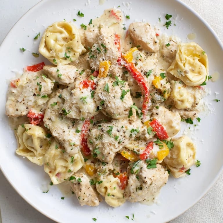 Close-up of vibrant Zesty Cajun Garlic Parmesan Chicken Tortellini; chicken pieces nestled in a rich sauce.