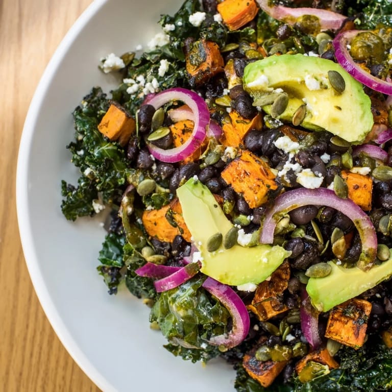 A close-up of a flavorful massaged kale salad with black beans, sweet potato, and crunchy pepitas.