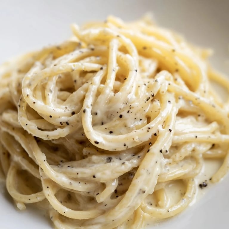 A close-up of Spaghetti Cacio e Pepe twirled on a fork, steam rising from the peppery, cheesy pasta.  