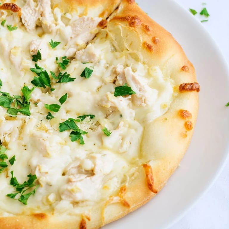 A slice of Chicken Alfredo Pizza being lifted, showing melted cheese stretch and a rich, creamy Alfredo sauce with tender chicken.