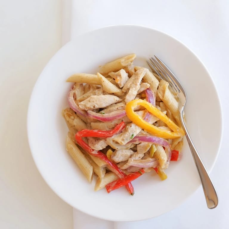Creamy Cajun Chicken Pasta Lite served in a white bowl, garnished with fresh parsley and red bell pepper slices for a colorful main dish.